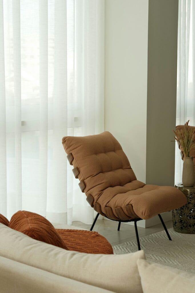 a modern comfy chair sits in the corner of a bright room next to a breezy curtain representing one type of traditional therapy that may work for some teens