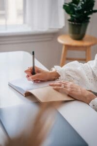 woman sitting at a white table journaling, tracking, scheduling