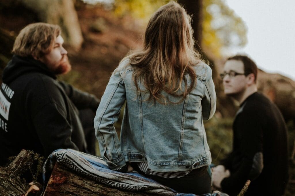 three people sit outside in a small circle discussing, representing how outdoor group therapy can be effective for teens