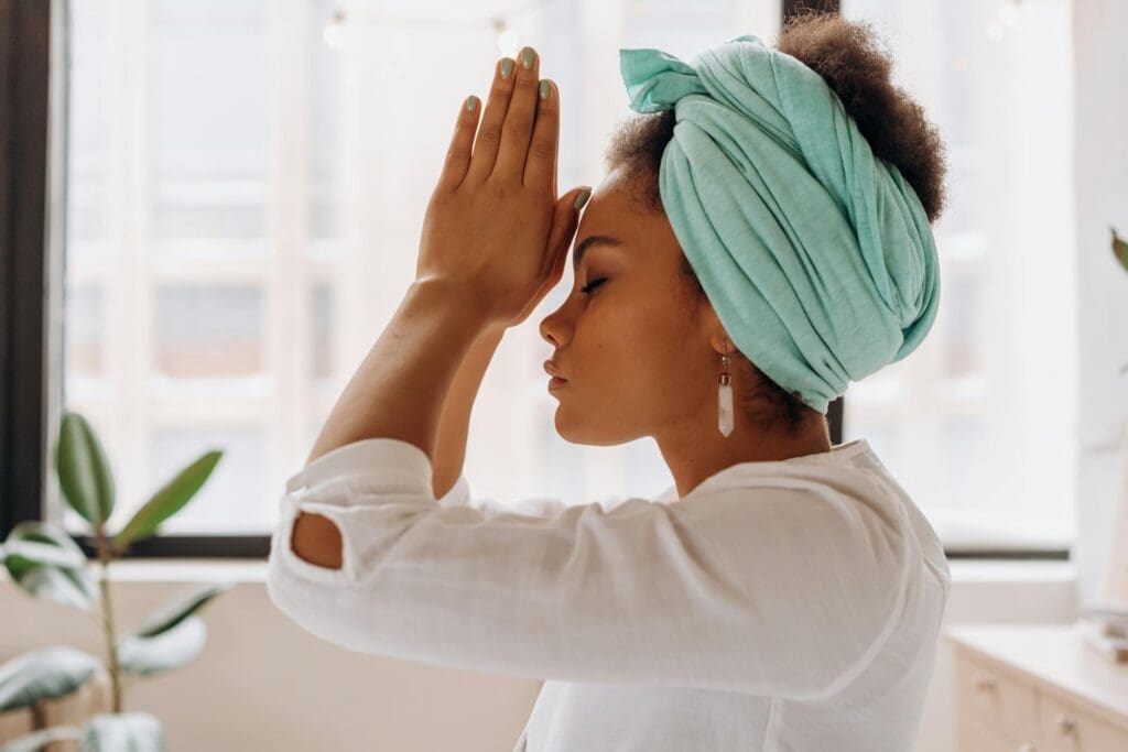 woman in white long sleeve shirt, eyes closed with hands in prayer or meditation position