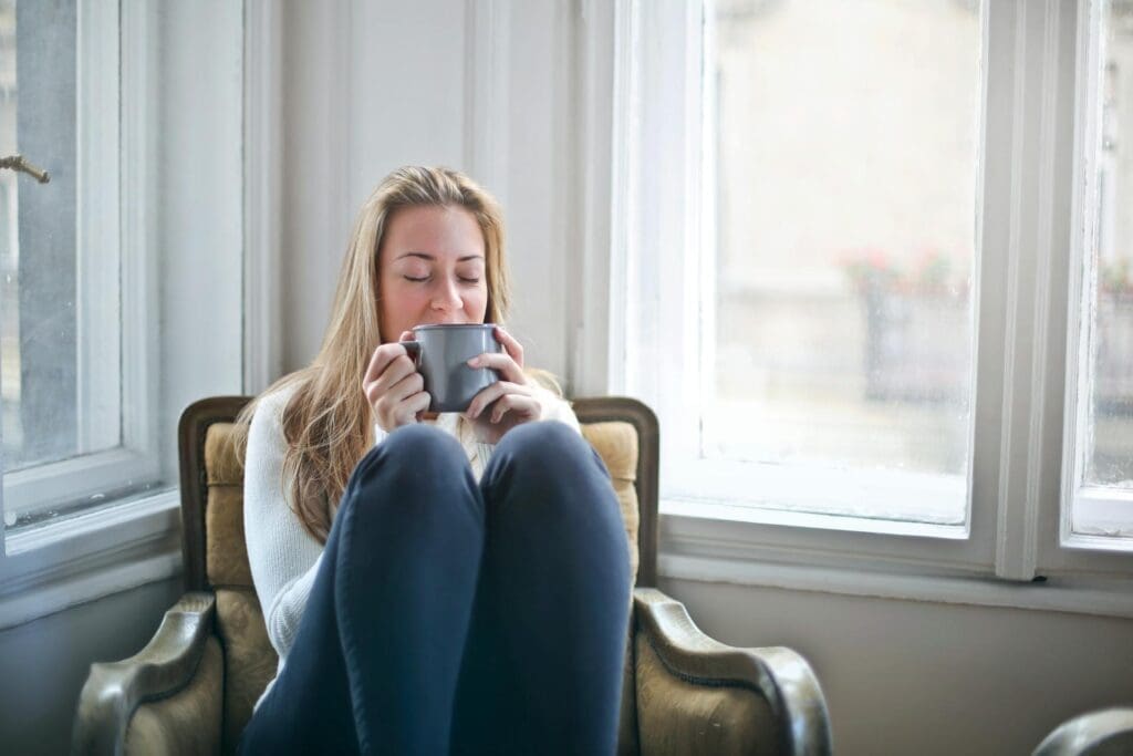 a person sits huddled in a chair holding a warm beverage with their eyes closed, an anxiety grounding technique in the 54321 method
