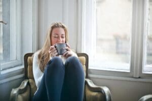 woman sitting comfortably in a chair, well-lit room, enjoying a warm drink, calm, relaxed