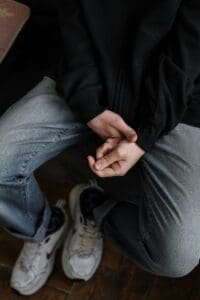 man sitting in chair, jeans, black sweatshirt, gripping hands, anxiety, anxiety therapy, therapy lifts weight of anxiety