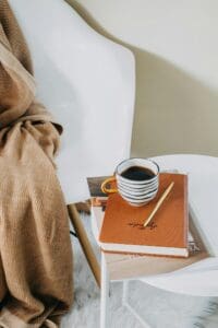white chair, brown blanket, cup of coffee, journal, pencil, therapy space