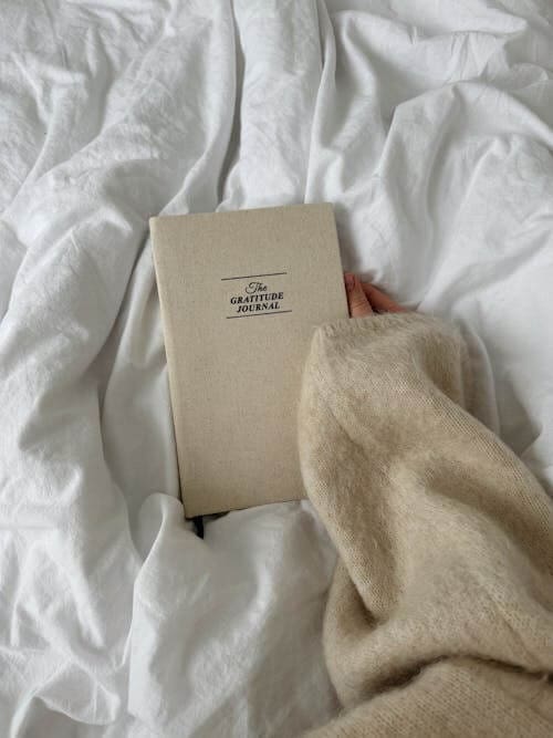 white comforter with a gratitude journal laying on it and a woman's hand reaching for it