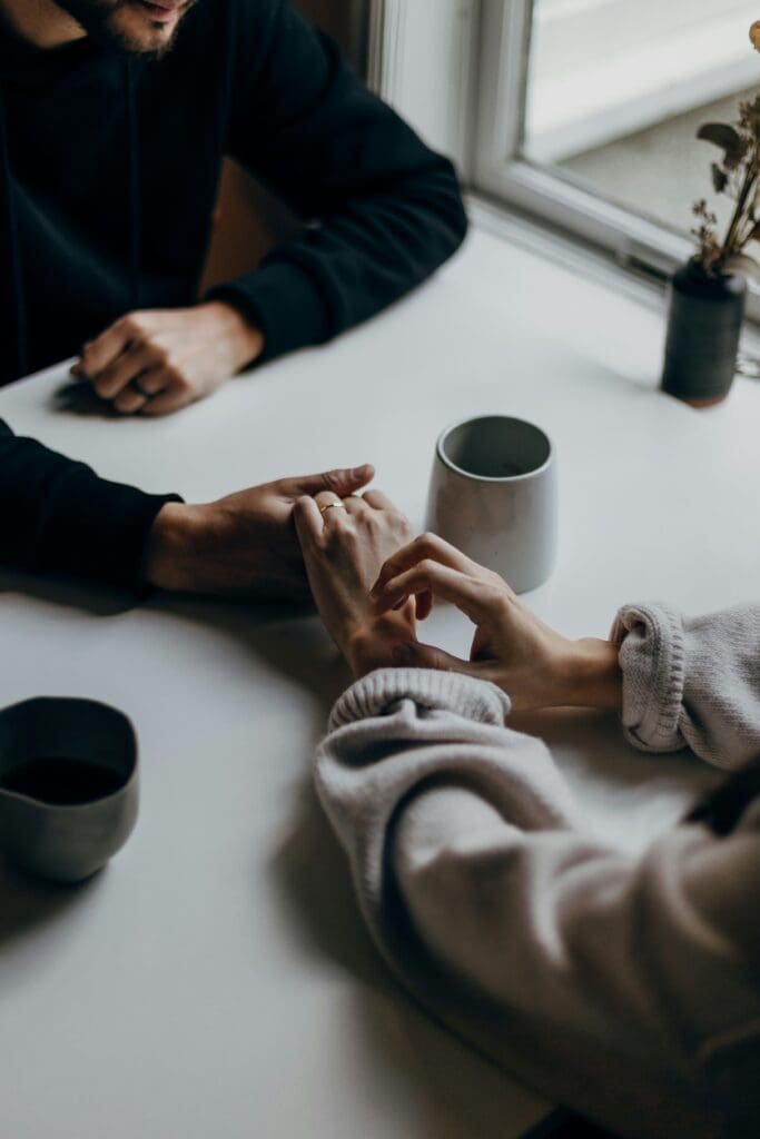 man and woman at a white table, holding hands across the table, cups of coffee