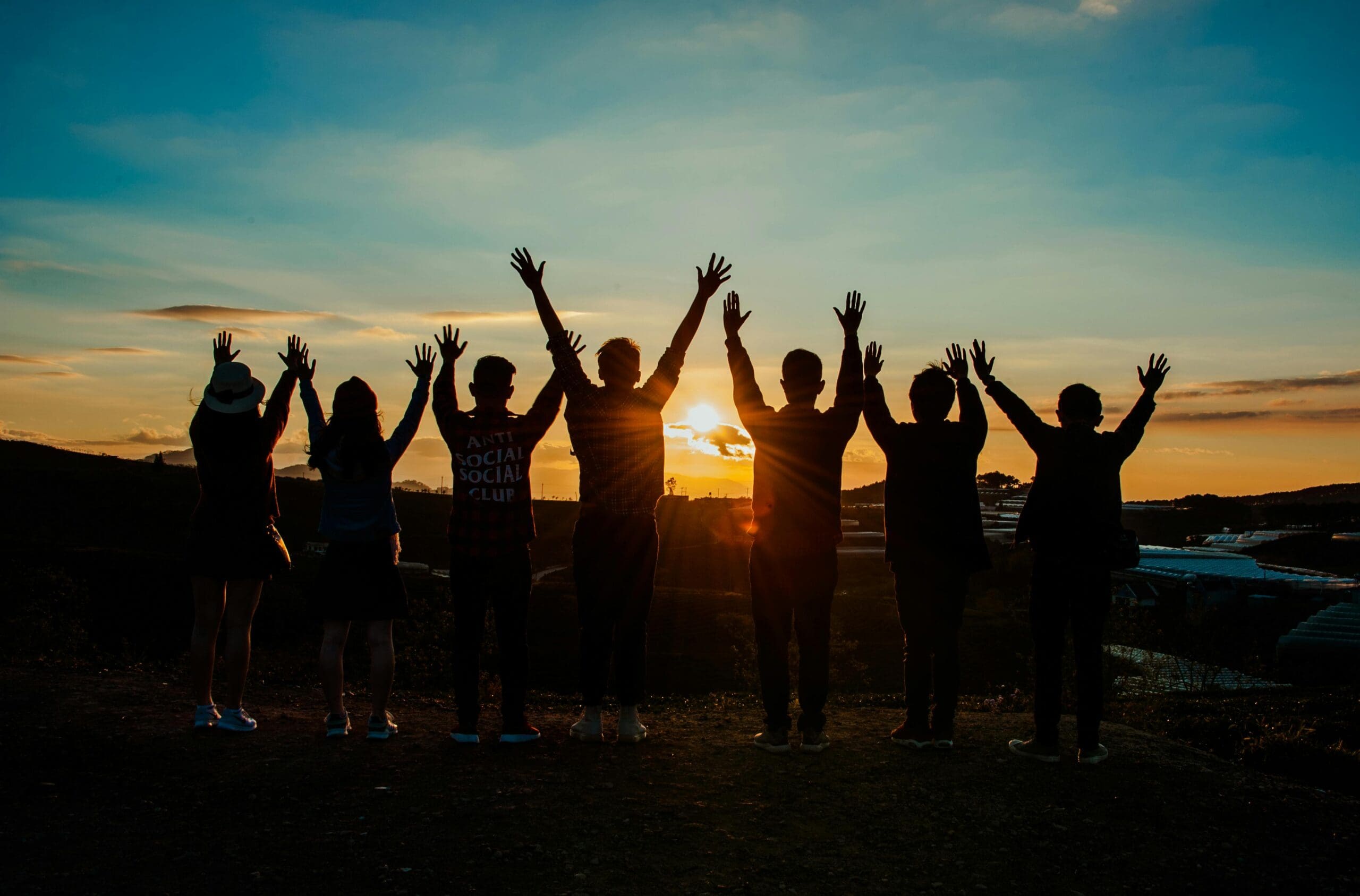 group of adults in nature, hands raised in the air admiring the sunset